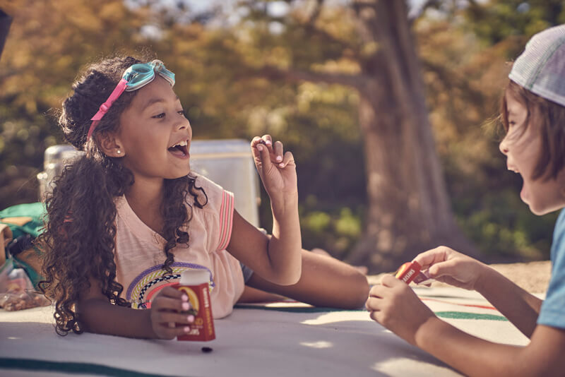 Two children sitting outdoors eating Sun-Maid raisins